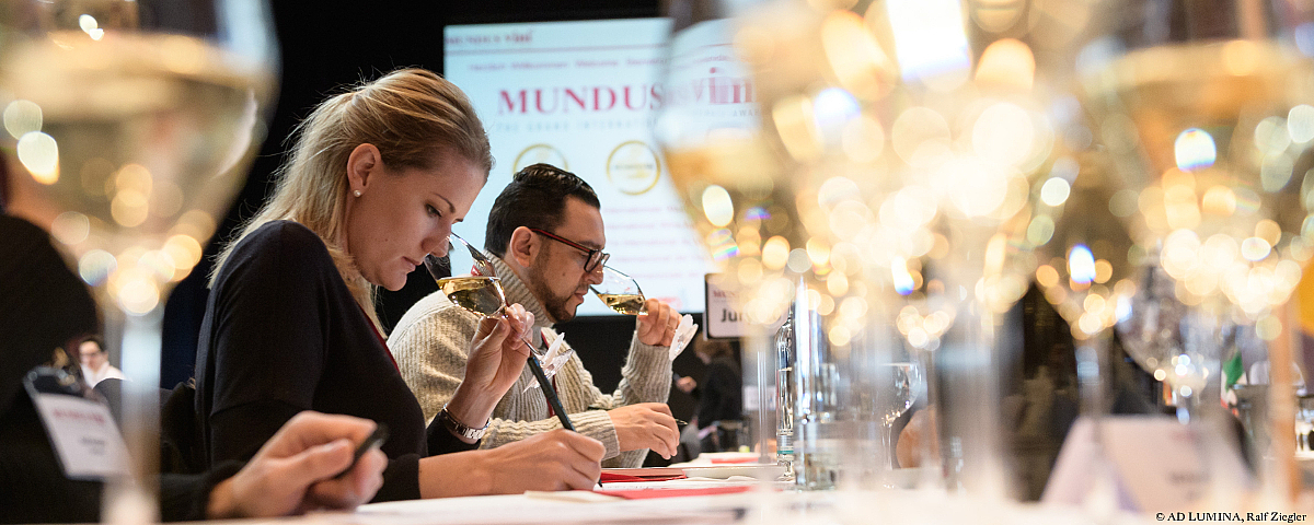 Jurymitglieder bei einer professionellen Weinverkostung von Mundus Vini, umgeben von gefüllten Weingläsern.