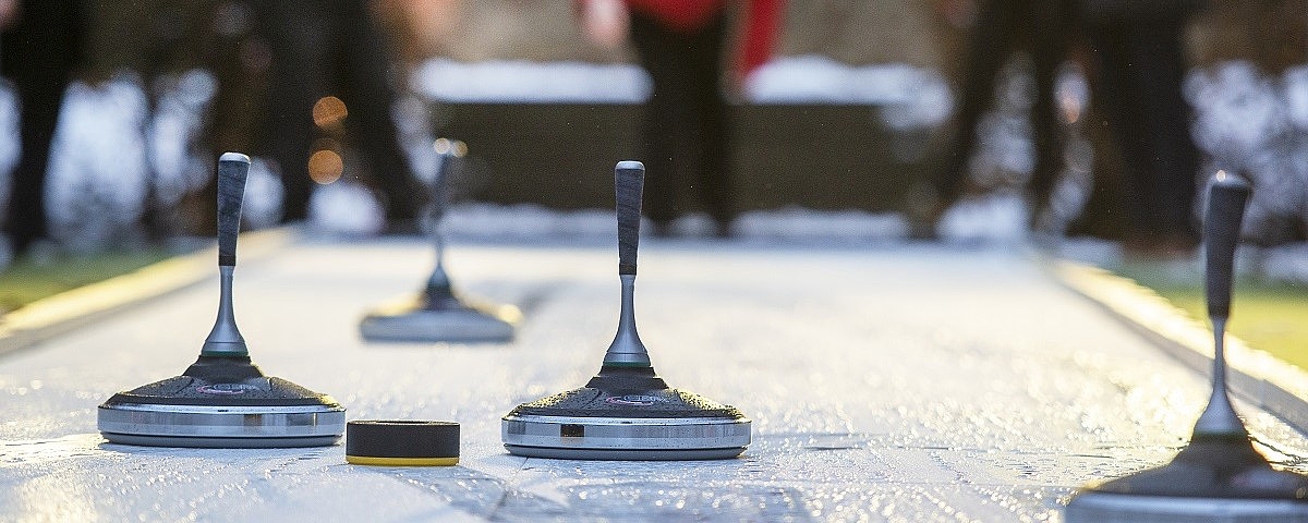 Mehrere Eisstöcke stehen auf einer Eisbahn, unscharfe Personen im Hintergrund bei einer Winterveranstaltung.