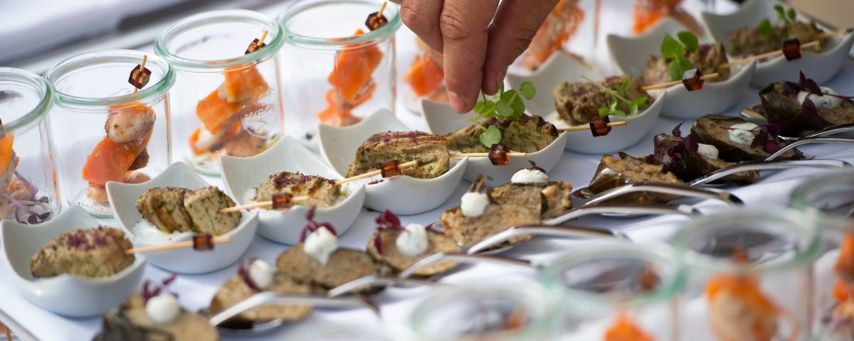 Selection of decoratively arranged finger food appetisers, including salmon skewers, nuts and herbs, arranged on a buffet.